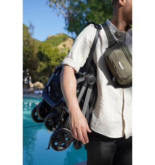 Person carrying colugo compact stroller folded and hanging on shoulder with an olive organizer across their chest