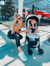 Woman and child in a stroller under a covered walkway with palm trees in the background.